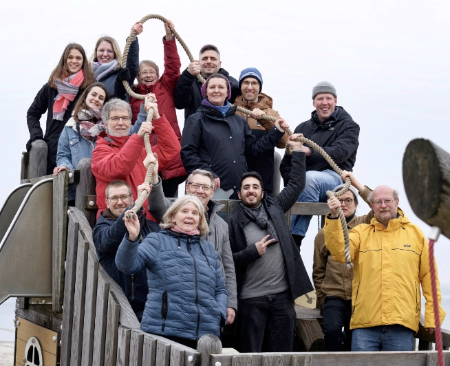 Mitarbeitende bei gemeinsamer Teamaktion am Strand mit Seilübung